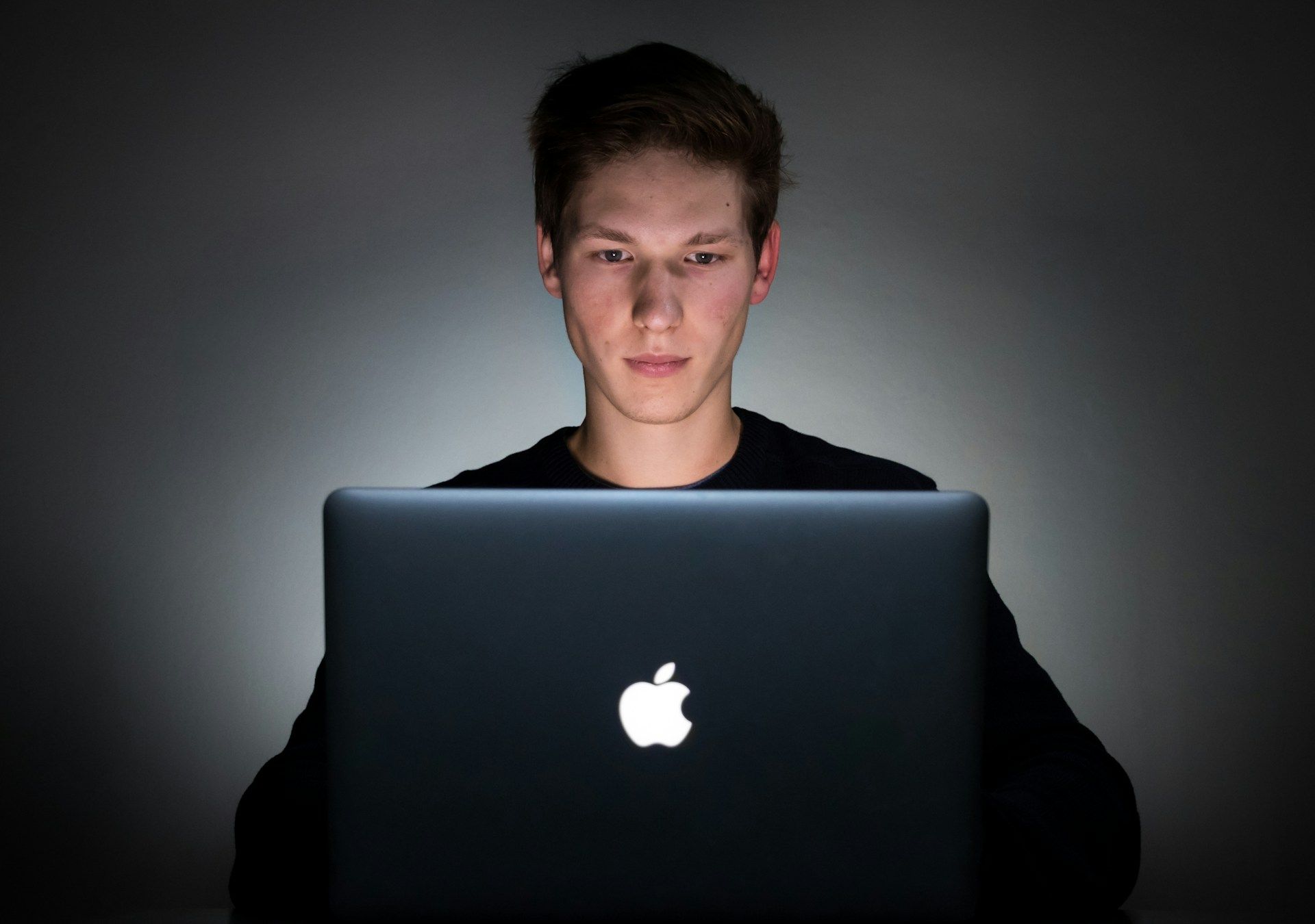 A serious young man using a laptop in the dark